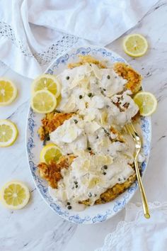 a white plate topped with food next to sliced lemons and a fork on top of a table