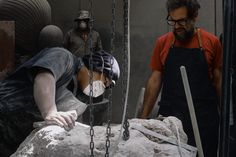 two men are working on a sculpture in the process of being made with chains and stone