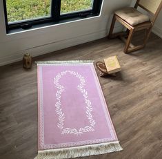 a pink rug sitting on top of a wooden floor next to a chair and window