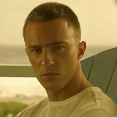 a young man sitting in a chair looking at the camera while wearing a white t - shirt