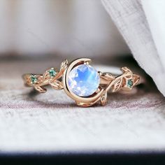 a ring with a blue stone surrounded by green stones and leaves on top of it