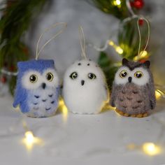 three small stuffed owls sitting on top of a table next to christmas lights and decorations