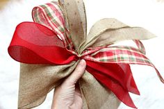 a hand holding a red ribbon wrapped in burlock on top of a white surface