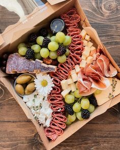 a box filled with assorted meats, cheese and fruit on top of a wooden table