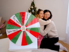 two women hugging each other in front of a christmas tree with a spinning wheel on it