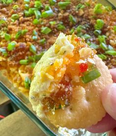 someone holding up a piece of food in front of a casserole dish