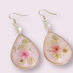 two pairs of earrings with flowers and pearls hanging from the ear hooks on a pink background