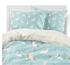 a bed with blue sheets and unicorns on it, along with white pillow cases