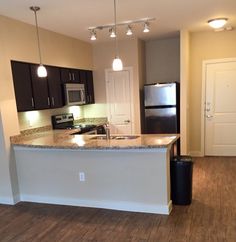 an empty kitchen and living room in a new home with wood flooring, stainless steel appliances and dark cabinets