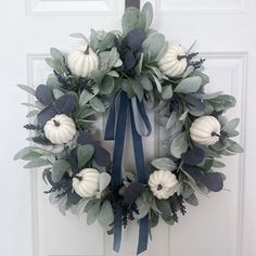 a wreath with white pumpkins and greenery hangs on the front door, next to a blue ribbon