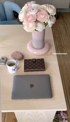 a laptop computer sitting on top of a wooden table next to a vase filled with flowers