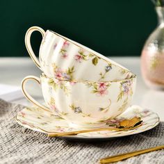 two cups and saucers sitting on a table next to a vase with pink flowers