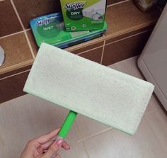 a person holding a sponge on top of a tile floor in front of a refrigerator