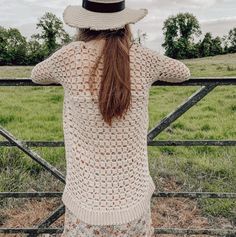 a woman standing in front of a fence with her back to the camera and wearing a hat