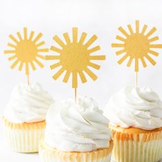 three cupcakes with white frosting and sun decorations on top, sitting next to each other