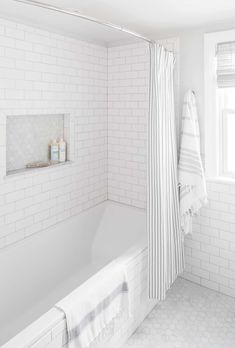 a white tiled bathroom with a tub and shower curtain