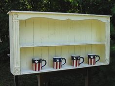 three coffee mugs are sitting on top of an old china cabinet with american flags painted on them