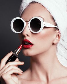 a woman with sunglasses and a towel on her head holding a lipstick in front of her face