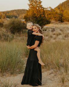 a woman holding a child in her arms while standing on top of a sandy beach