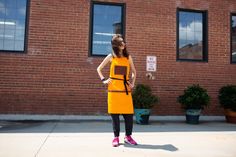 a woman standing in front of a brick building wearing an orange dress and pink tennis shoes