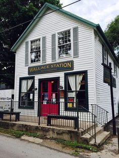 a small white building with a red door and black fence around it's entrance