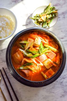 a bowl of soup with tofu, green beans and other foods on the side