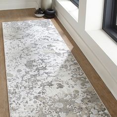 a white and gray rug in front of a window with a vase on the floor