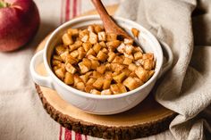 a bowl filled with food sitting on top of a wooden cutting board next to an apple