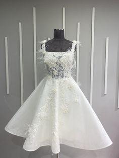 a white dress with feathers on the skirt and neckline is displayed in front of a mannequin