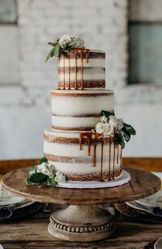 a three tiered cake with white flowers and chocolate drizzled on top