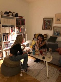 two women sitting on couches in a living room with bookshelves behind them