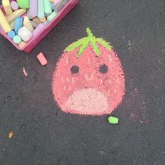 a child's chalk drawing of a strawberry on the ground next to crayons