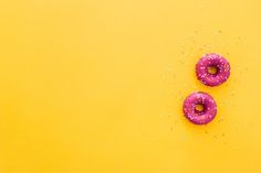 two pink doughnuts sitting on top of a yellow surface with sprinkles