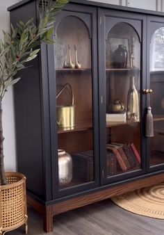 a black china cabinet sitting on top of a hard wood floor next to a potted plant