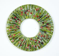 a green and red glass wreath on a white surface with beads in the center,