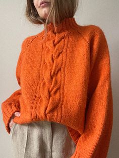 a woman in an orange sweater is standing with her hands on her hips and looking off to the side