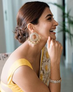 a woman in a yellow dress smiling and wearing large earrings on her left earring