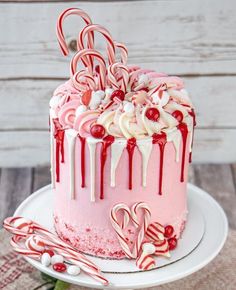 a pink cake with white icing and candy canes on top is sitting on a plate