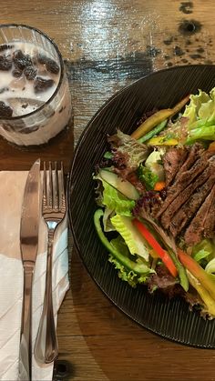 a steak salad with lettuce and carrots on a plate next to a drink