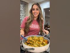 a woman in a pink shirt holding a pan filled with food