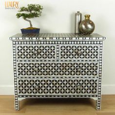 a white and black patterned dresser next to a potted plant