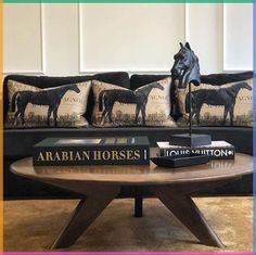 a coffee table with books on it in front of a couch and horse head pillows