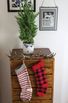 two christmas stockings hanging on a dresser next to a potted plant and framed pictures