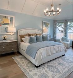 a bedroom with blue walls and white bedding, chandelier, two lamps, dressers and chairs