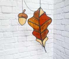 a stained glass leaf and acorn hanging from a chain on a white brick wall