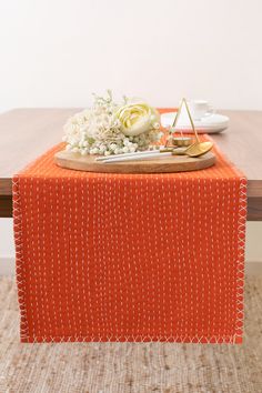 an orange table runner on top of a wooden table with white flowers and goldware