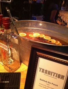 a table topped with a metal bowl filled with liquid and lemons next to a framed sign