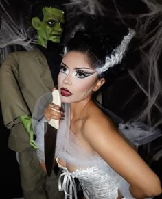 a woman in white dress holding a knife next to a man wearing green mask and costume