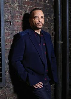 a man standing in front of a brick wall wearing a blue suit and red shirt