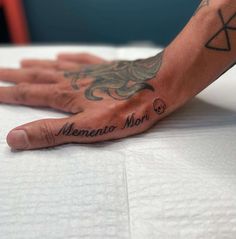 a person's hand with tattoos on it sitting on top of a white sheet